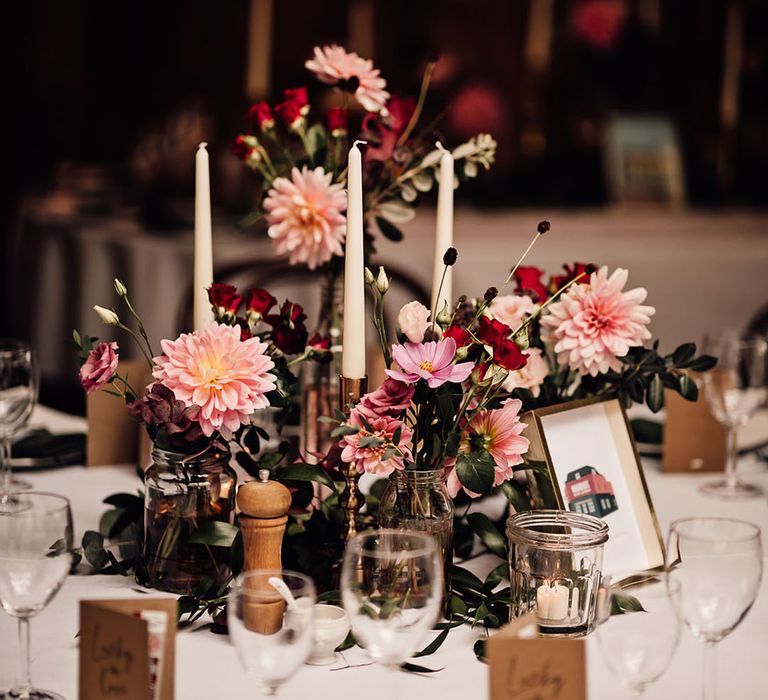 Bud vases full of pink and red wedding flowers and white taper candles for the centrepieces 