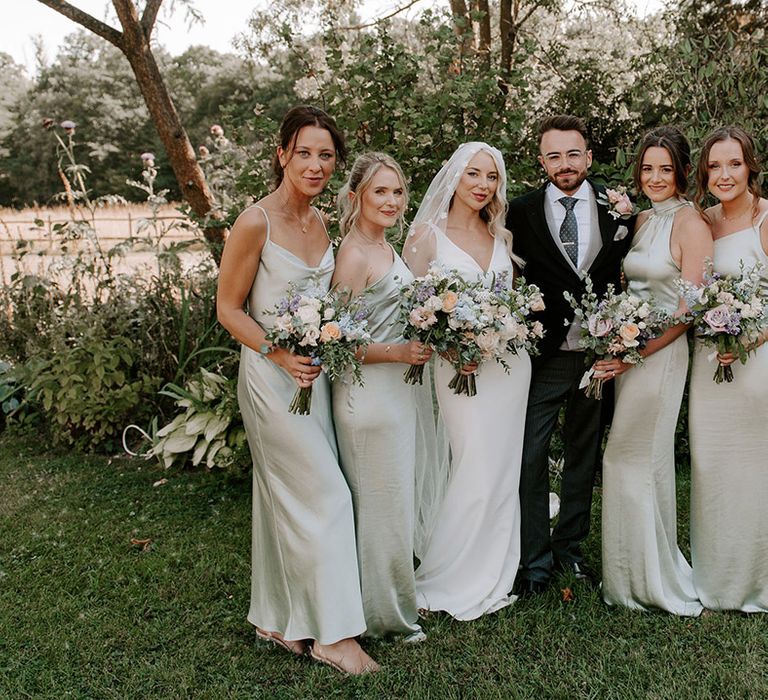 Groom in three piece suit with the bride in a Made With Love wedding dress with bridesmaids in sage green dresses in mismatched styles 