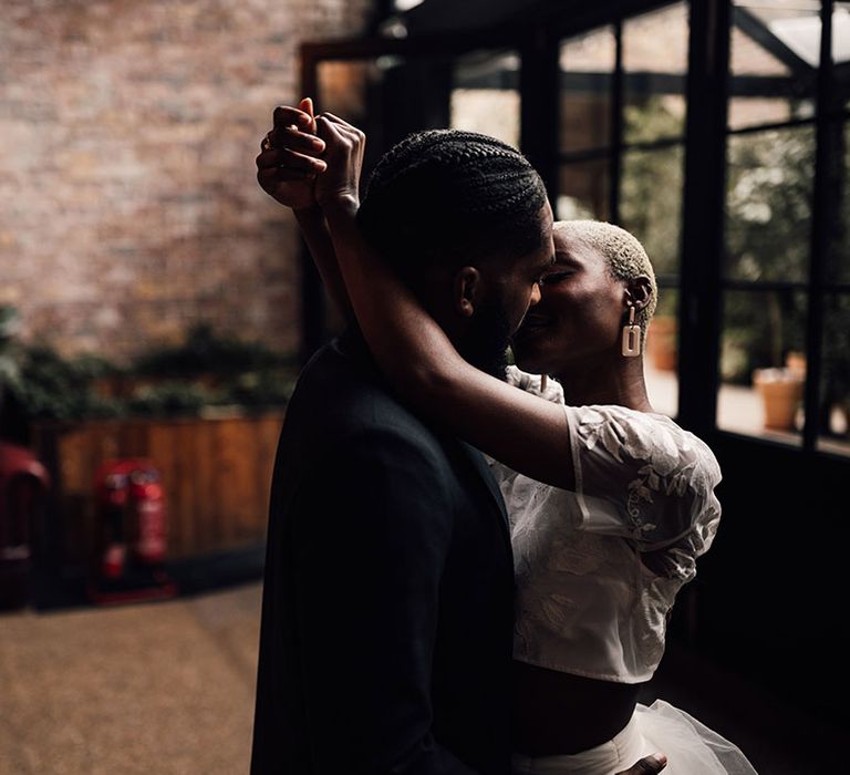 Black Bride and Groom share a kiss at 100 Barrington Wedding Venue. The Bride wears a bridal two piece set and statement earrings for her wedding jewellery