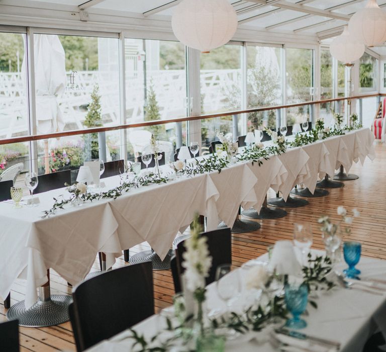 Banquet table with white tablecloth and green foliage decor to the front 