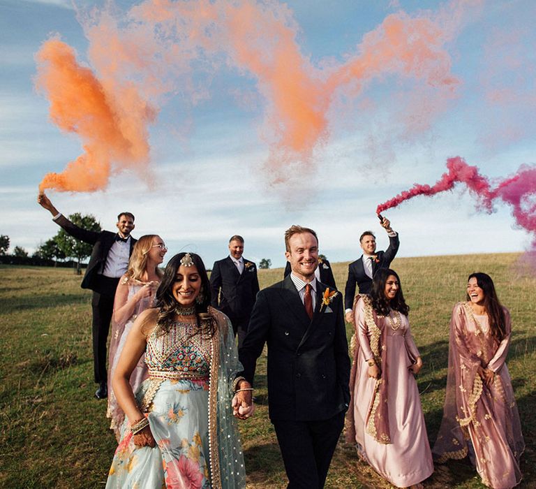 Bride & groom walk alongside their wedding party with colourful smoke bomb portraits 