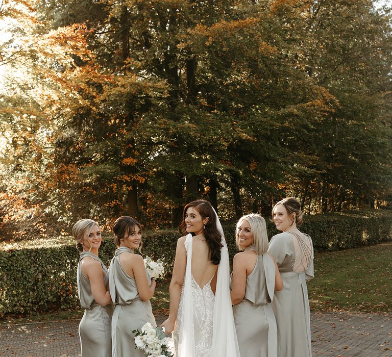 Bride in an open back wedding dress with watteau train with her bridal party wearing sage green satin bridesmaid dresses 