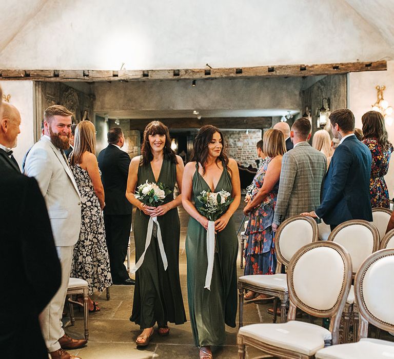 Bridesmaids in green bridesmaid dresses walking down the aisle together holding white flower bouquets 