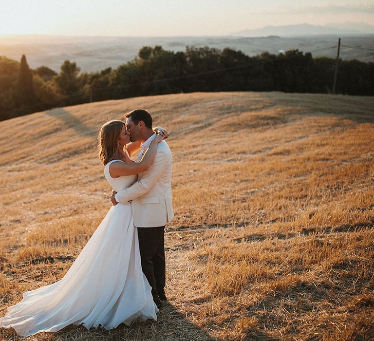 Bride & groom kiss in field during outdoor couples portraits with golden hour sunshine 