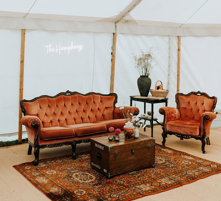 Furniture seating area in the marquee with red velvet sofas and custom made neon wedding sign