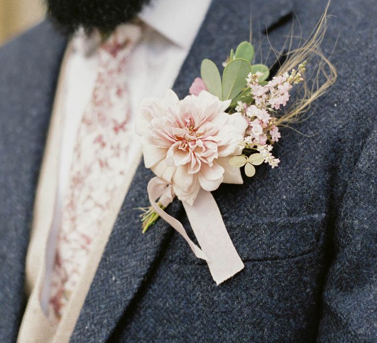 Groom in dark blue suit with floral pink patterned tie with pink flower buttonhole tied with pink ribbon and foliage 