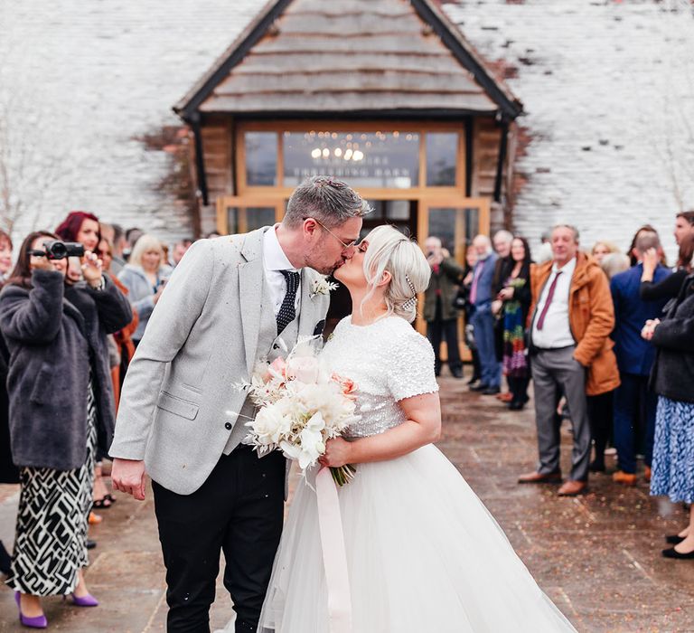 Bride wearing short sleeve beaded top and tulle bridal skirt kissing the groom after their wedding ceremony 