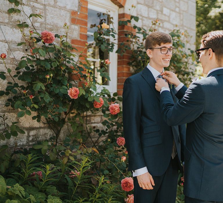 The groomsman helps the groom with the finishing touches for his wedding outfit by fixing on the buttonhole 