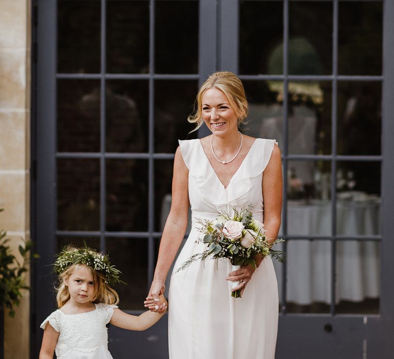 Bridesmaid in white bridesmaid dress walking along with the flower girl in a white dress at outdoor ceremony 