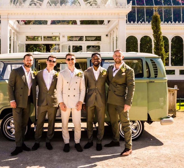 Groomsmen in double breasted dark green suits with the groom in a cream matching suit in front of the green camper van wedding transport 