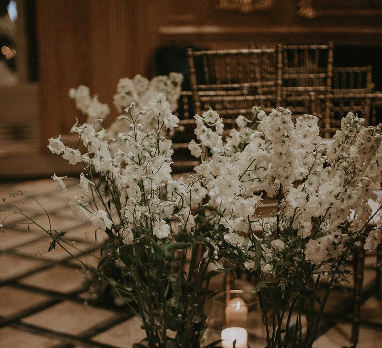 Pretty and extravagant white wedding flower aisle decoration with white pillar candles in vases