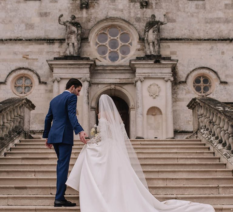 Bride in sparkly long sleeve off the shoulder wedding dress with groom in blue suit for luxury wedding 