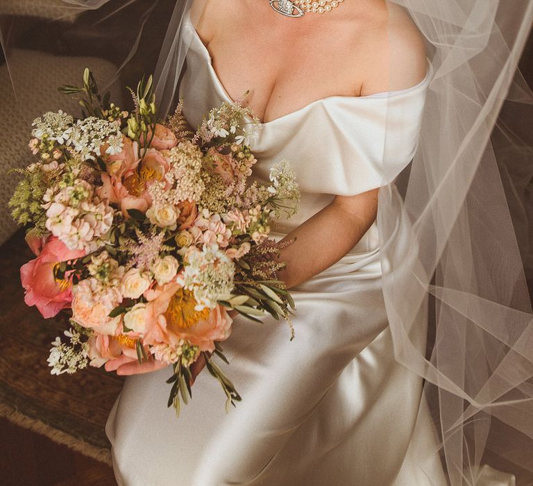 Bride in off the shoulder Vivienne Westwood wedding dress with pearl choker necklace and wedding veil with pink and white flower bouquet