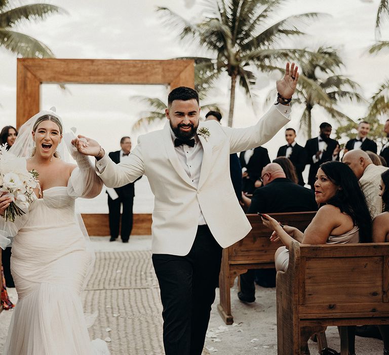 modern blue venado beach wedding ceremony with bride in a strapless tulle wedding dress and groom in a white dinner jacket descending up the aisle as husband and wife