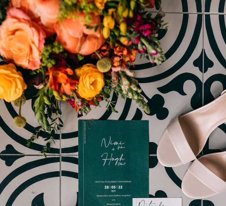 Contemporary wedding stationery on patterned floor with open toe blush wedding heels and colourful bridal flower crown