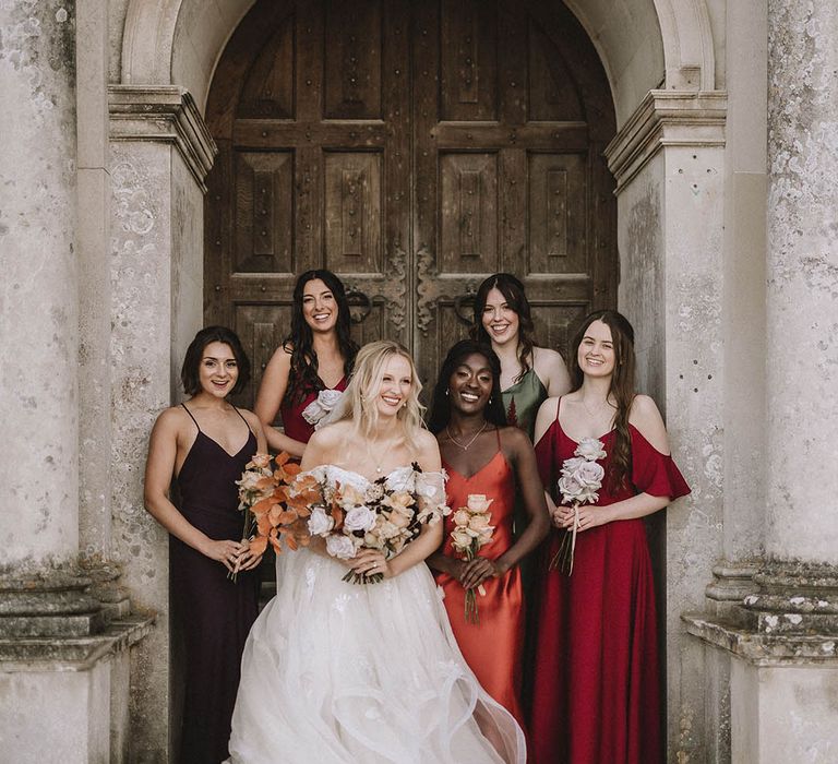 Castle wedding featuring bridesmaids in satin gowns in different fall colours and bride in princess wedding dress