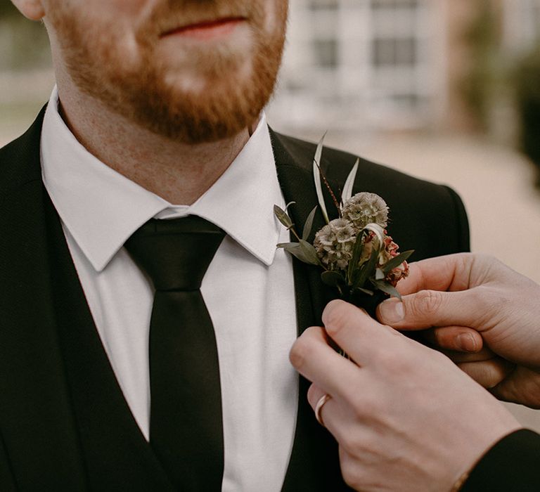 Wedding buttonhole being attached to the groom's wedding suit 