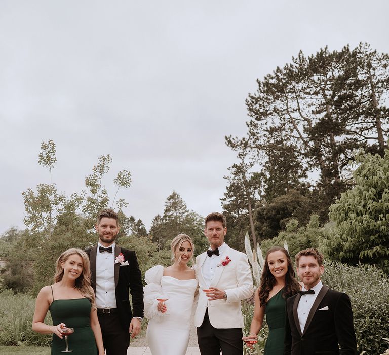 Groomsmen in black tuxedos,  bridesmaids in green bridesmaid dresses with the groom in a white tux and bride in satin gown 