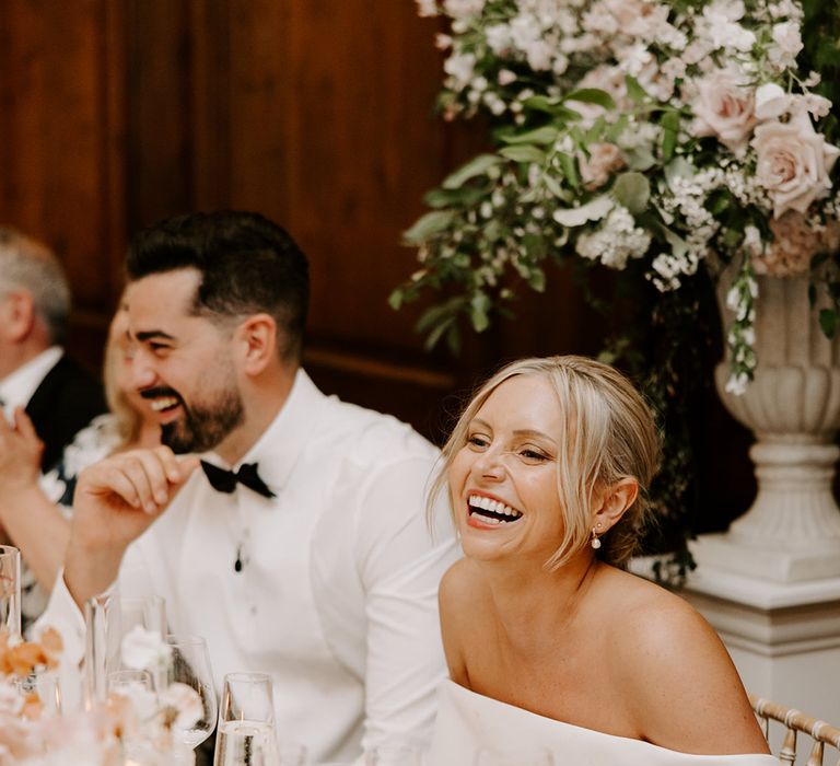 Bride and groom sitting at their wedding breakfast laughing at the wedding speeches 