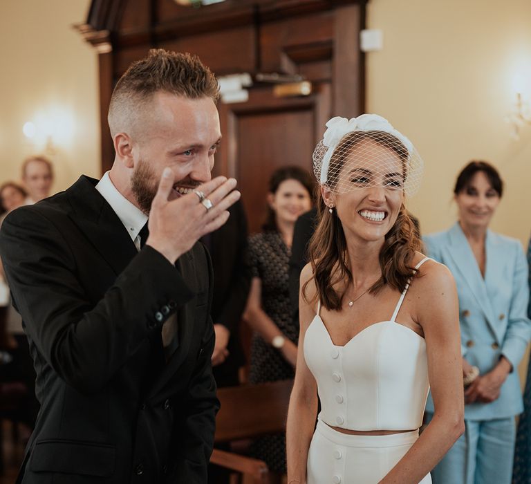 groom in a black suit laughing during the Chelsea town hall registry office wedding ceremony 