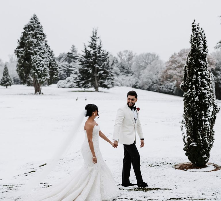 Snowy wedding at Hedsor House country house wedding venue with the bride and groom walking through the winter landscape 