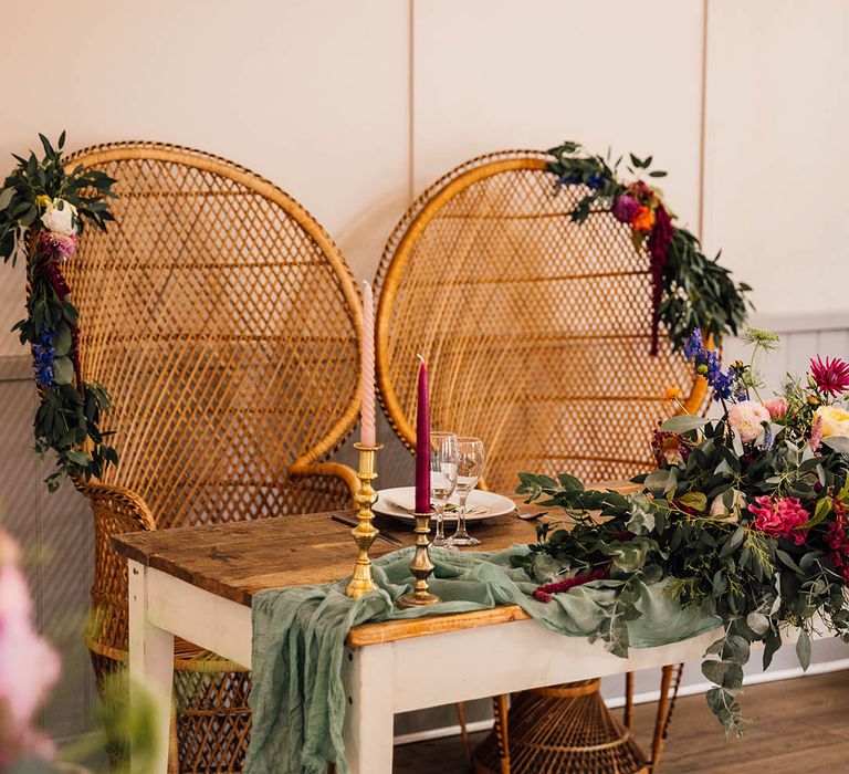 Sweetheart wedding table with two boho peacock chairs with foliage decor and colourful flowers 