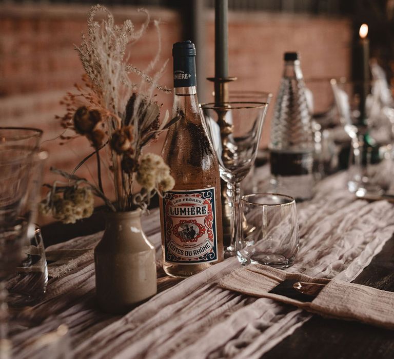 Gold rimmed glassware, white wedding table runner and bottle of wine decorate the wooden tables 