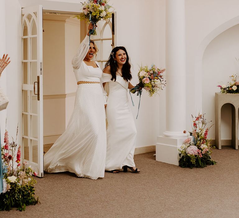 Two brides celebrate as they enter their wedding reception together at Pennsylvania Castle Estate venue 