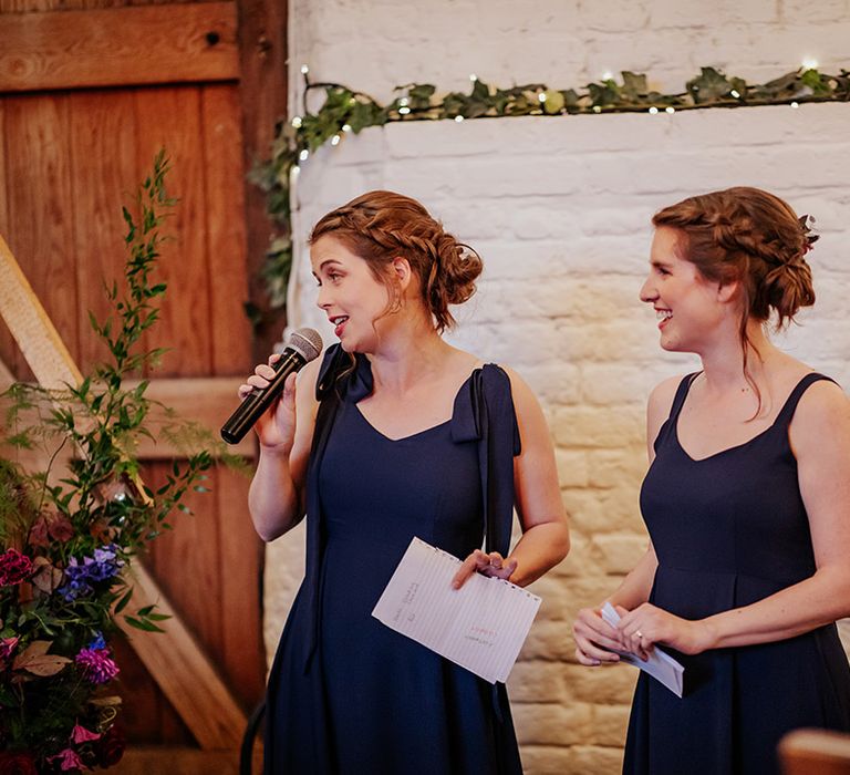 The two bridesmaids wearing navy blue bridesmaid dresses reading their joint wedding speech 