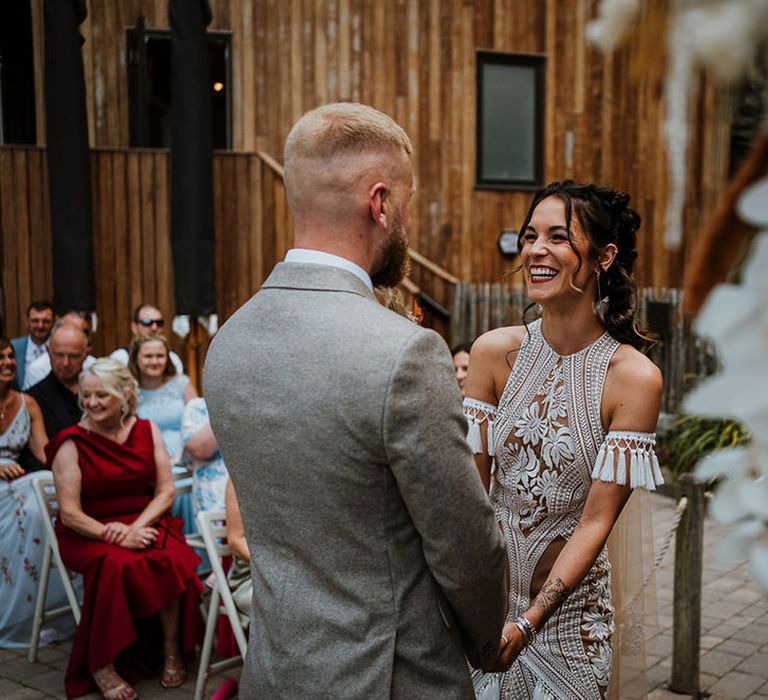 Bride and groom facing each other holding hands at their outdoor costal wedding ceremony 