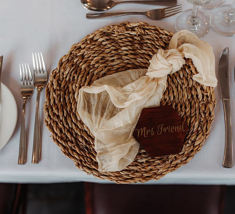 Wicker place mat with sheer white wedding napkin and burgundy wedding place name table setting 