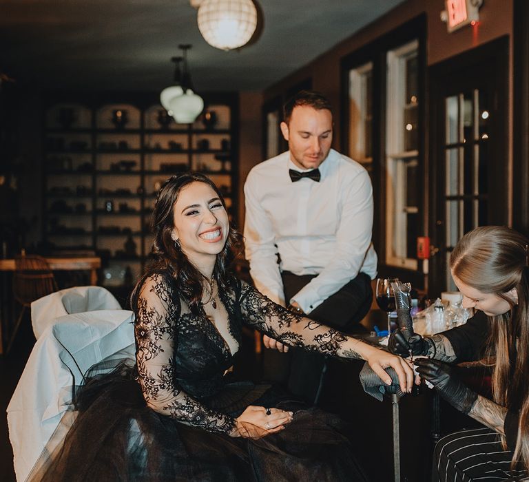 The bride sits getting tattooed in place of wedding rings 