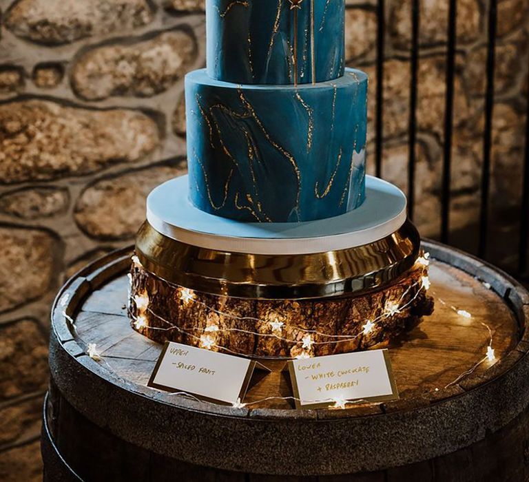 Two tier navy blue iced wedding cake with shimmery gold detailing and crescent moon cake topper for celestial wedding 