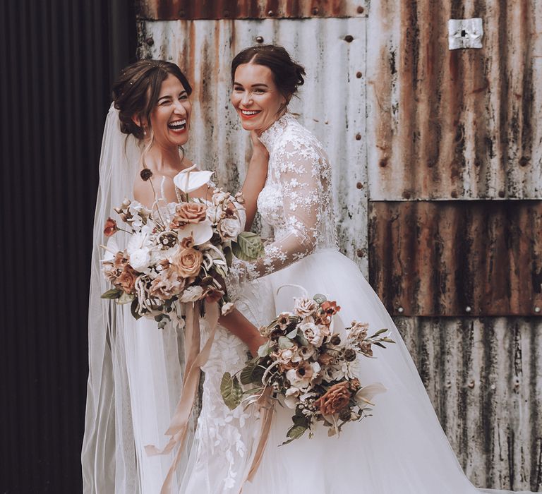 Two brides smiling as they pose for their couple portraits carrying neutral wedding bouquets 