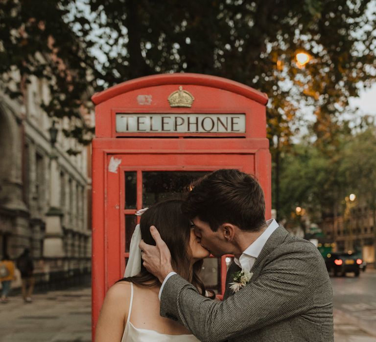 Bride and groom kissing next to a red telephone box 