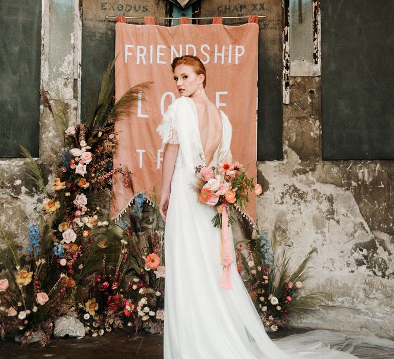 Bride in V back dress holding a colourful bouquet at The Asylum altar 