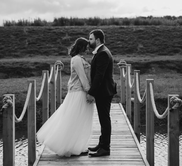 Bride in denim jacket holding hands with groom on a bridge