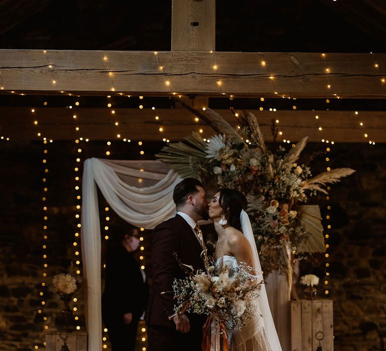 Bride and Groom kiss at boho wedding with fairy lights and pampas grass