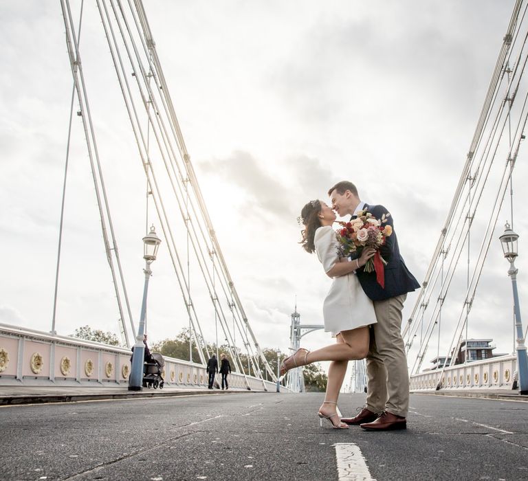 Bride in short wedding dress and Sophia Webster shoes standing on a bridge in London with her groom 