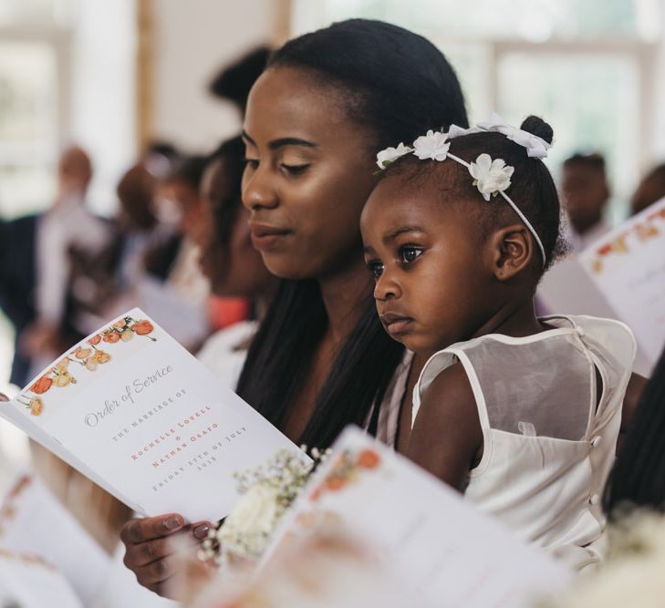 Bridesmaid holding a DIY order of service and a flower girl with flower headdress