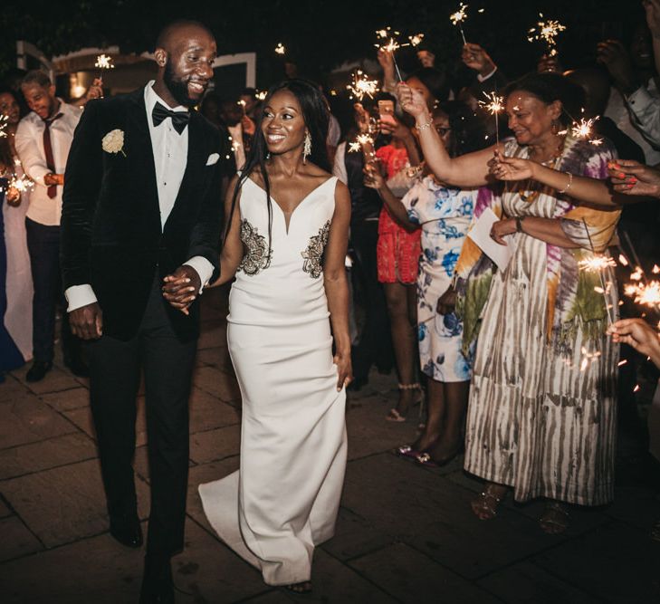 Sparkler moment with the Black bride in a fitted wedding dress with waist detail holding her grooms hand in a black tuxedo 