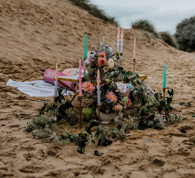 Twisted colourful candles in gold candlestick holders and pastel flower arrangements for intimate picnic on the beach 