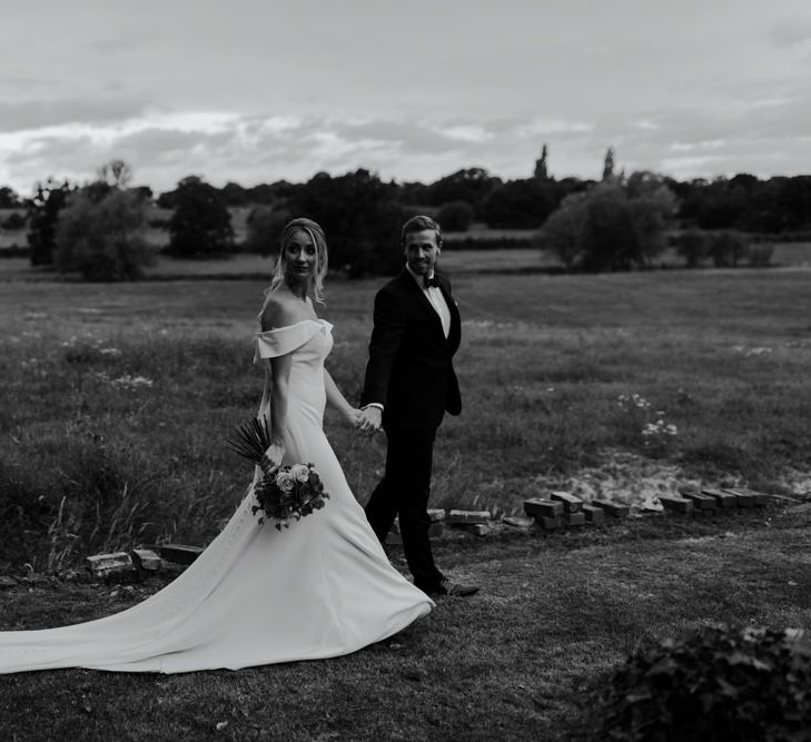 Black & white image of bride and groom walking within the countryside