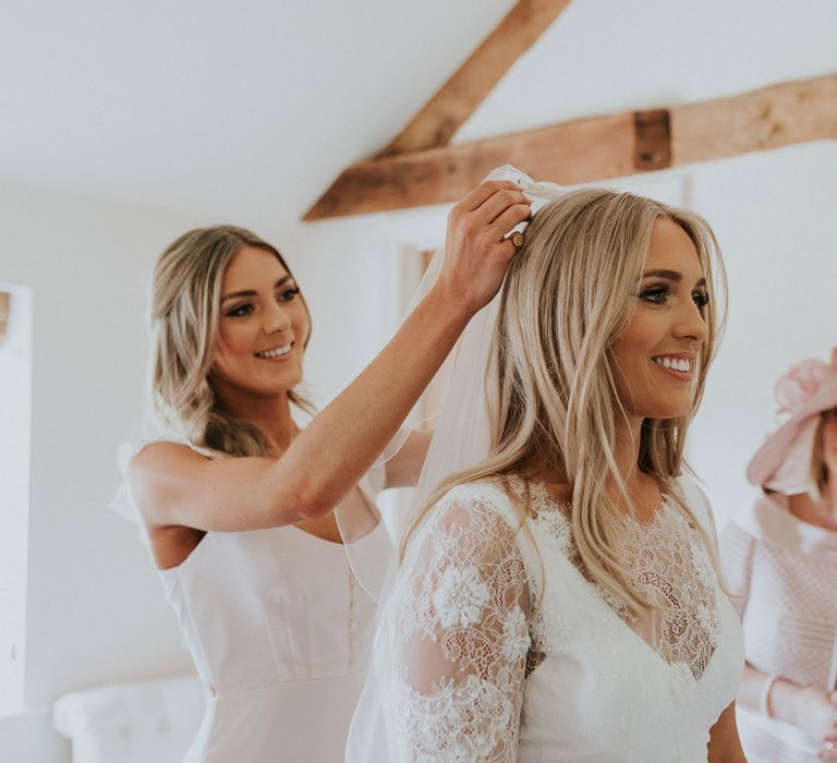 Bridesmaid in silk ivory button dress puts veil on bride in white Charlie Brear wedding dress and white Augusta Jones lace top