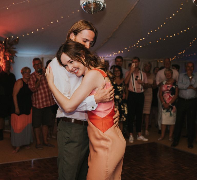 Bride & groom embrace during first dance whilst bride wears orange reception dress