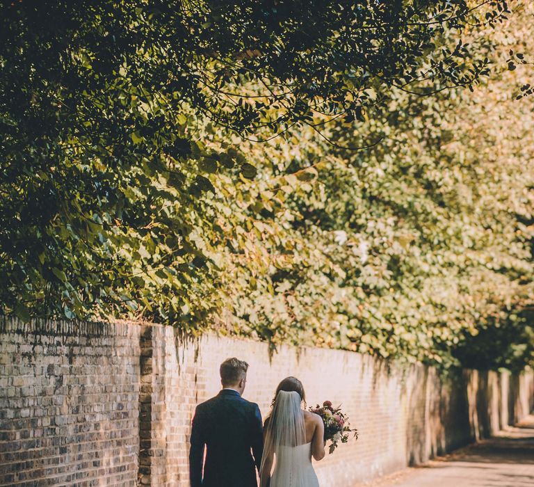 Bride and groom outside photography from behind, bride wears fishtail ruffled wedding dress and groom wears Navy suit