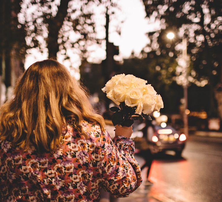 Bride holds up white rose bouquet as she walks through Chelsea