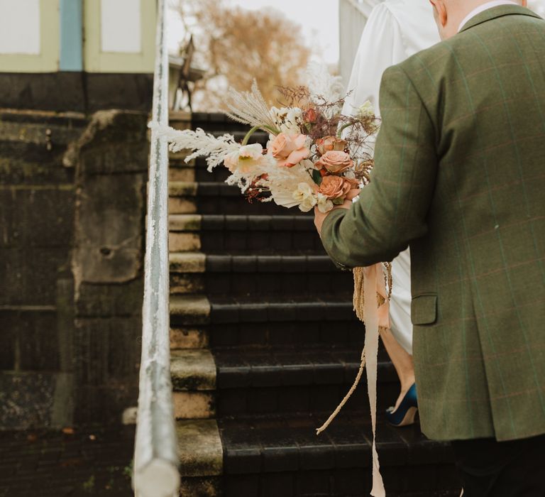 Groom wears tweed jacket and carries floral bouquet