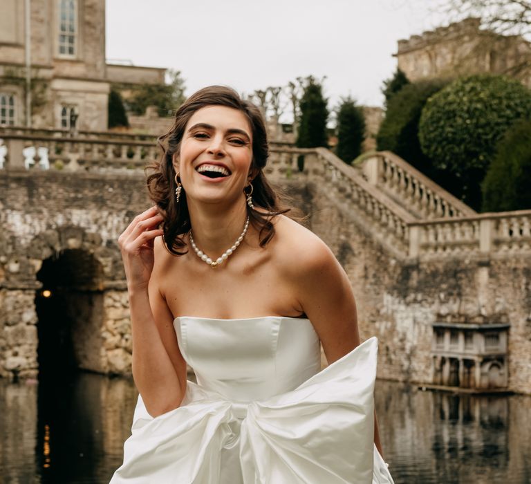 Bride laughs and wears short wedding gown with large bow and pearl necklace 