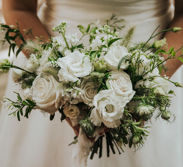 White floral bouquet with white roses, peonies and green foliage held by bride